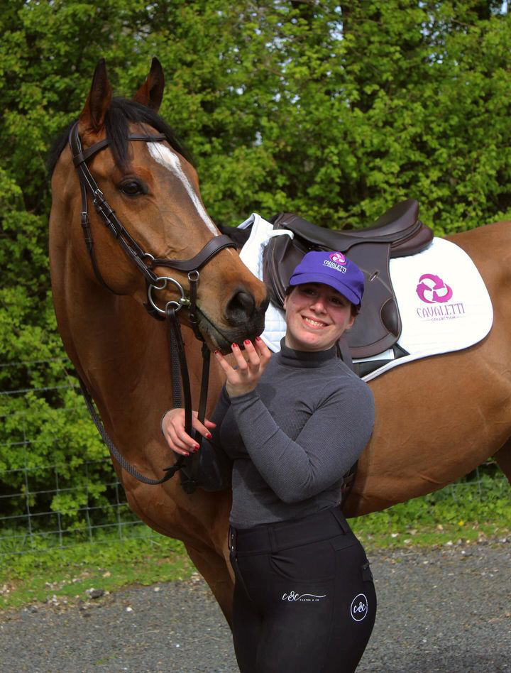 Equestrian rider smiling with horse wearing Cavaletti Collection white saddle pad and branded gear outdoors.